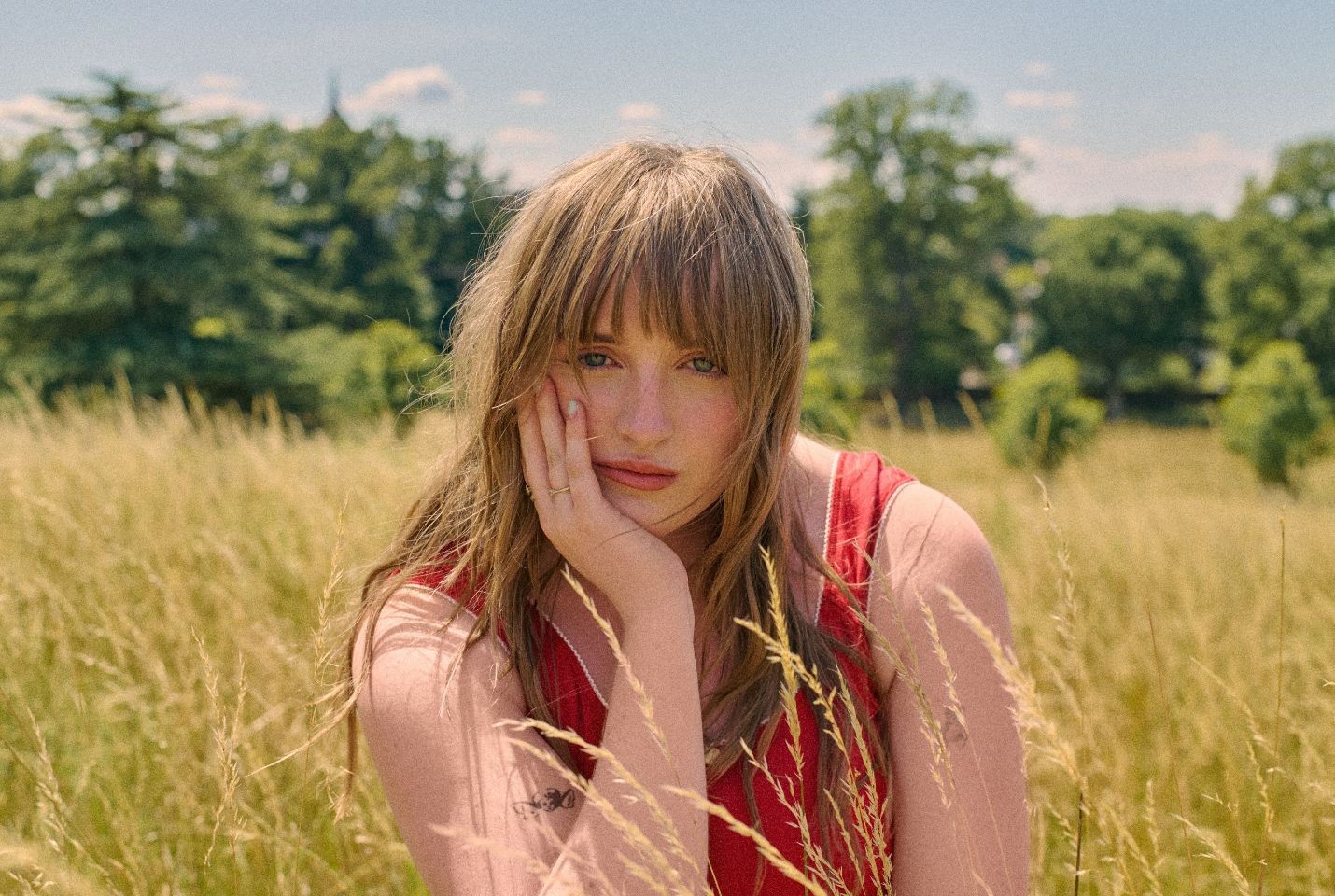 A woman in a red top with brown hair sat in a field